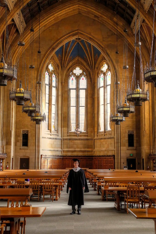 Vaulted library ceilings rise above the graduate.